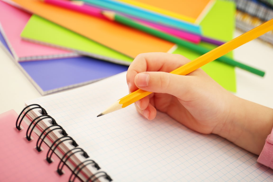 Child's Hand Writing on a Notebook with a Pencil